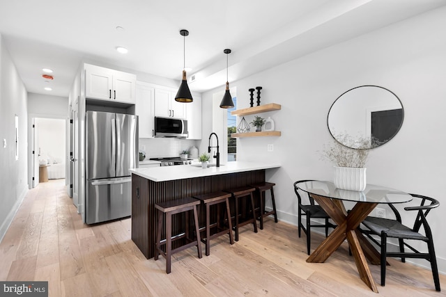 kitchen with a breakfast bar, white cabinets, light wood-type flooring, appliances with stainless steel finishes, and kitchen peninsula