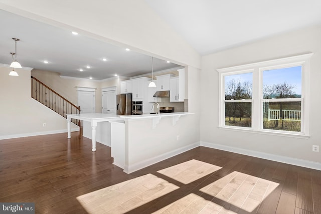 kitchen featuring appliances with stainless steel finishes, white cabinets, dark hardwood / wood-style floors, hanging light fixtures, and a breakfast bar area