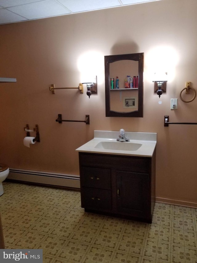 bathroom with a paneled ceiling, vanity, toilet, and a baseboard heating unit