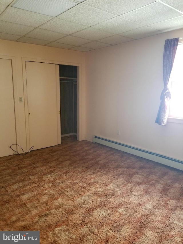 unfurnished bedroom featuring carpet flooring, a drop ceiling, a closet, and a baseboard radiator