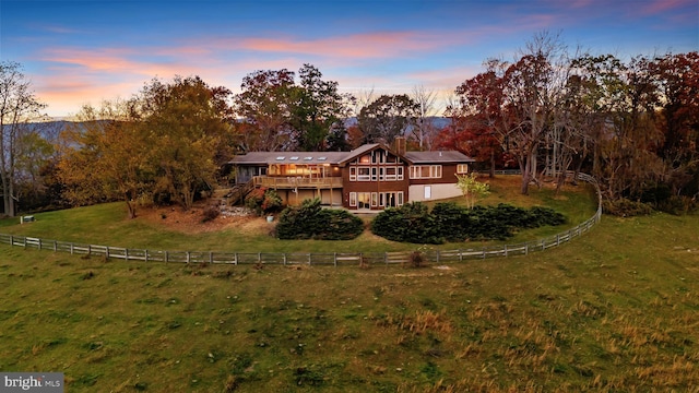 back house at dusk with a yard, a rural view, and a wooden deck