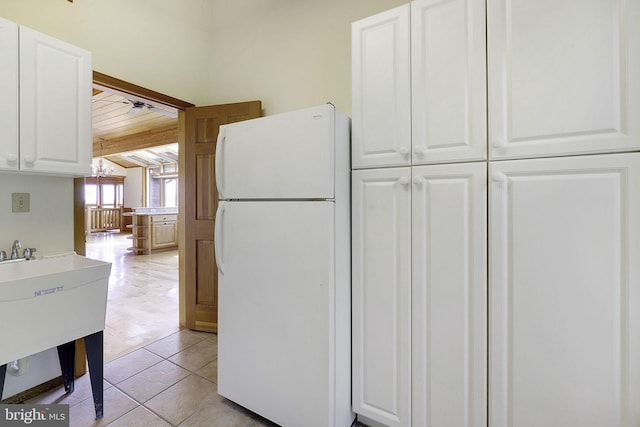 kitchen with white refrigerator, light tile patterned flooring, white cabinetry, and sink