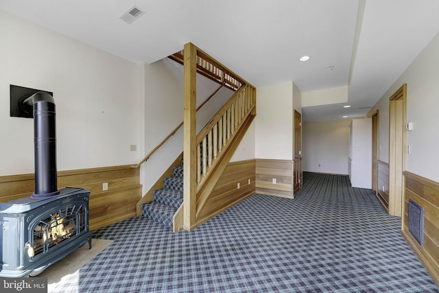 stairs featuring wood walls, a wood stove, and carpet floors