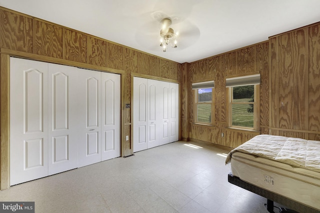 bedroom with ceiling fan, wooden walls, and two closets