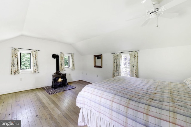 bedroom with ceiling fan, wood-type flooring, a wood stove, and lofted ceiling