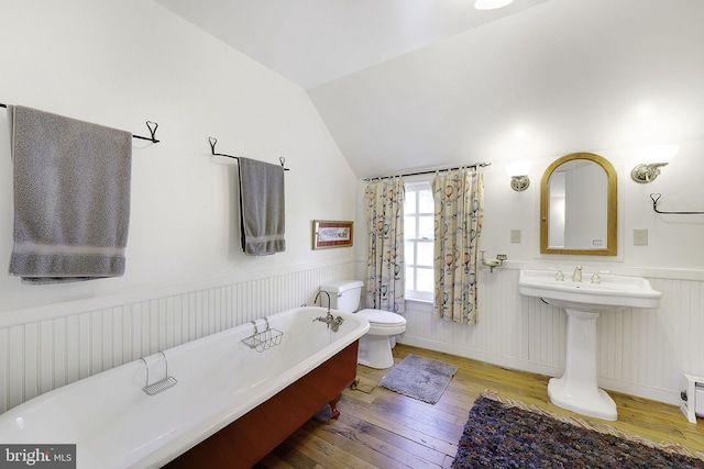 bathroom featuring a bathtub, wood-type flooring, vaulted ceiling, and toilet