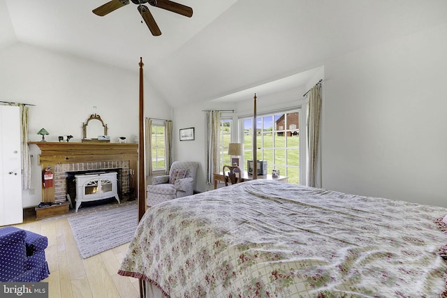 bedroom with ceiling fan, light hardwood / wood-style floors, lofted ceiling, and a wood stove