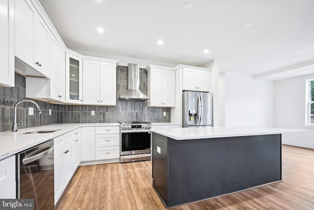 kitchen featuring light hardwood / wood-style floors, appliances with stainless steel finishes, wall chimney exhaust hood, white cabinets, and sink