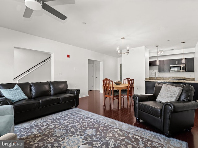 living area featuring ceiling fan with notable chandelier, baseboards, and wood finished floors