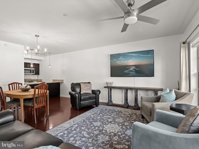 living area featuring baseboards, wood finished floors, and ceiling fan with notable chandelier