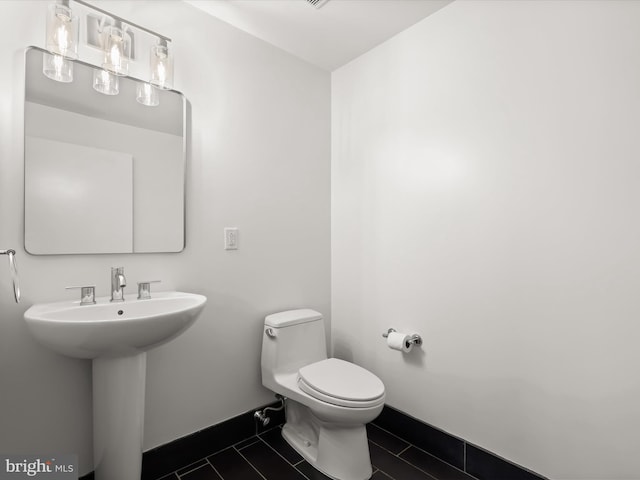 half bathroom featuring a sink, baseboards, toilet, and tile patterned flooring