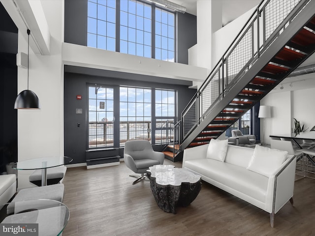 living room with stairs, wood finished floors, baseboards, and a towering ceiling