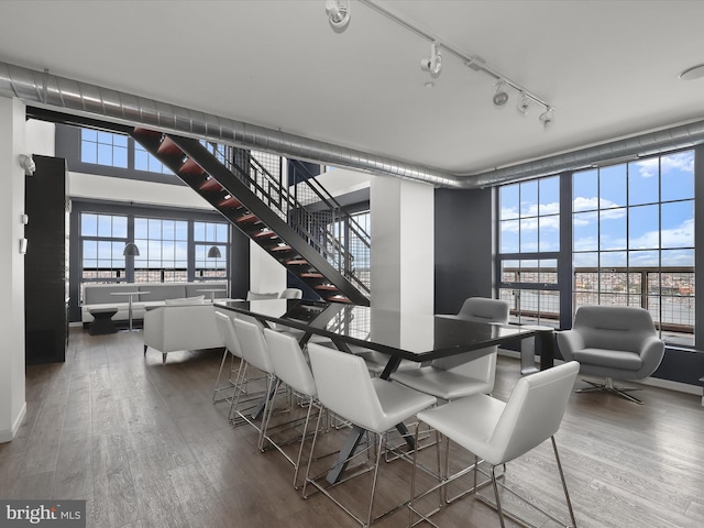 dining area with a wall of windows, plenty of natural light, wood finished floors, and stairs