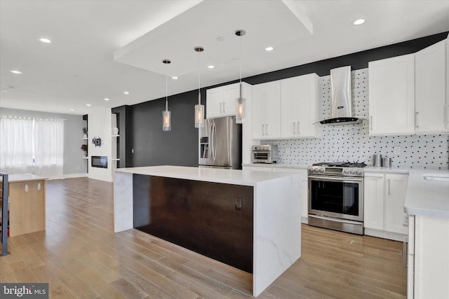 kitchen featuring appliances with stainless steel finishes, light hardwood / wood-style floors, white cabinetry, and wall chimney range hood