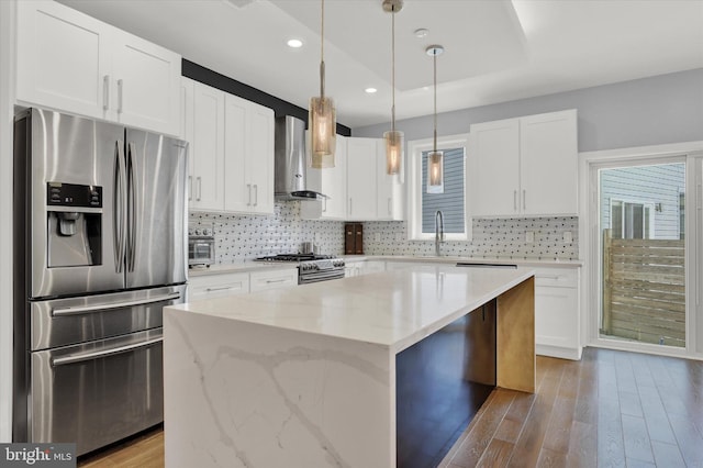 kitchen featuring light wood-type flooring, wall chimney exhaust hood, stainless steel appliances, white cabinets, and a kitchen island