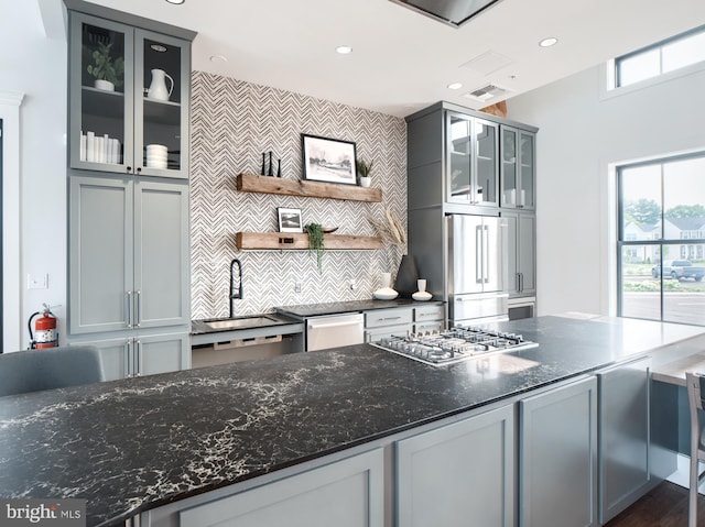 kitchen with gray cabinets, appliances with stainless steel finishes, tasteful backsplash, dark stone counters, and sink