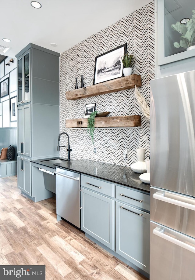 kitchen featuring appliances with stainless steel finishes, tasteful backsplash, light wood-type flooring, dark stone counters, and sink