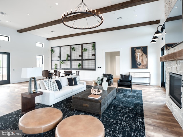 living room featuring light wood-type flooring, a chandelier, a fireplace, and beamed ceiling