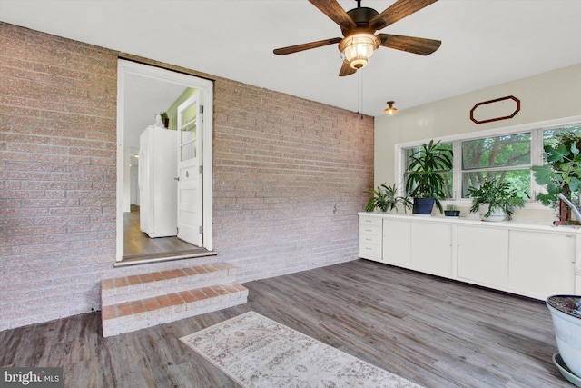 interior space with ceiling fan, brick wall, and dark hardwood / wood-style floors