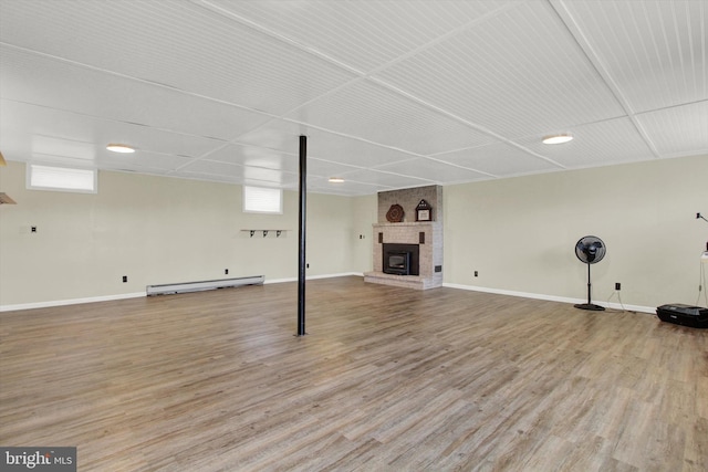 basement with a brick fireplace, a paneled ceiling, light hardwood / wood-style floors, and a baseboard radiator