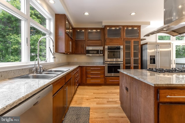 kitchen featuring sink, light stone counters, light wood-type flooring, island exhaust hood, and stainless steel appliances