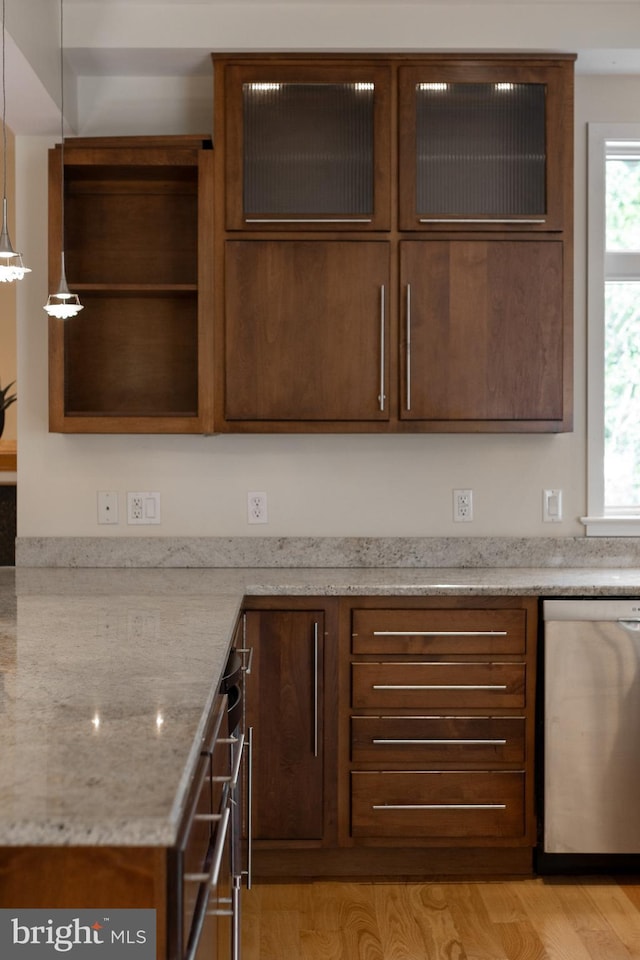 kitchen with pendant lighting, stainless steel dishwasher, light stone countertops, and light wood-type flooring