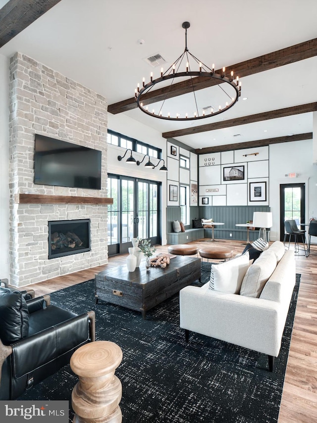 living room featuring beamed ceiling, hardwood / wood-style flooring, a stone fireplace, and plenty of natural light