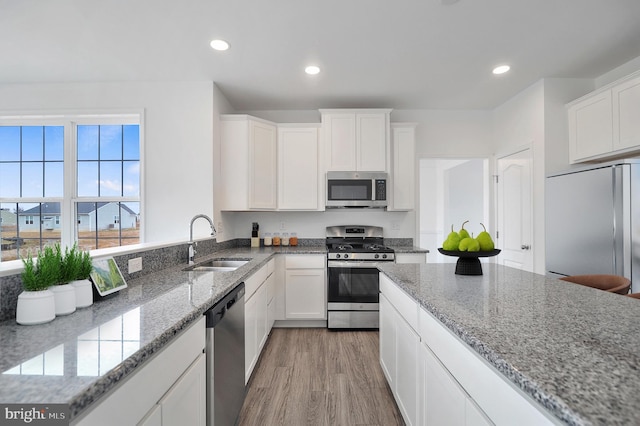 kitchen with light stone countertops, sink, appliances with stainless steel finishes, white cabinets, and light wood-type flooring