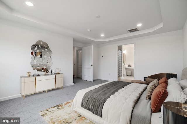 carpeted bedroom featuring ensuite bathroom and a raised ceiling