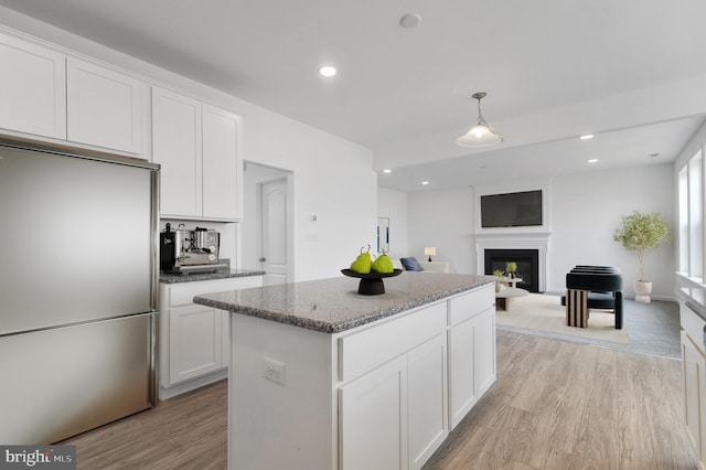 kitchen with light stone counters, light hardwood / wood-style flooring, stainless steel fridge, decorative light fixtures, and white cabinets