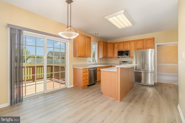 kitchen featuring sink, hanging light fixtures, light hardwood / wood-style flooring, appliances with stainless steel finishes, and a kitchen island