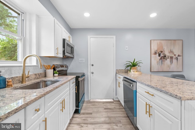 kitchen featuring stainless steel appliances, white cabinets, light stone counters, and sink