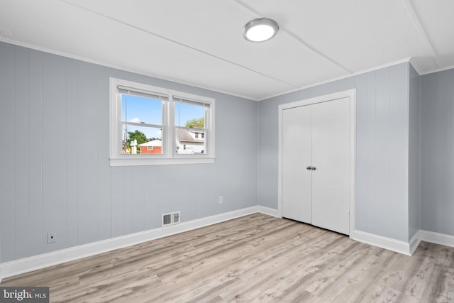 unfurnished bedroom with a closet, ornamental molding, wooden walls, and light wood-type flooring