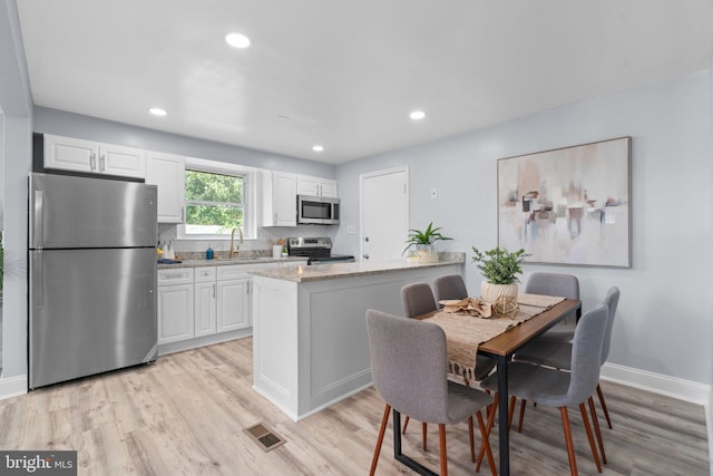 kitchen featuring light stone countertops, white cabinets, appliances with stainless steel finishes, sink, and light hardwood / wood-style flooring