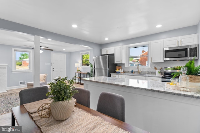 kitchen featuring sink, light wood-type flooring, appliances with stainless steel finishes, white cabinets, and light stone counters