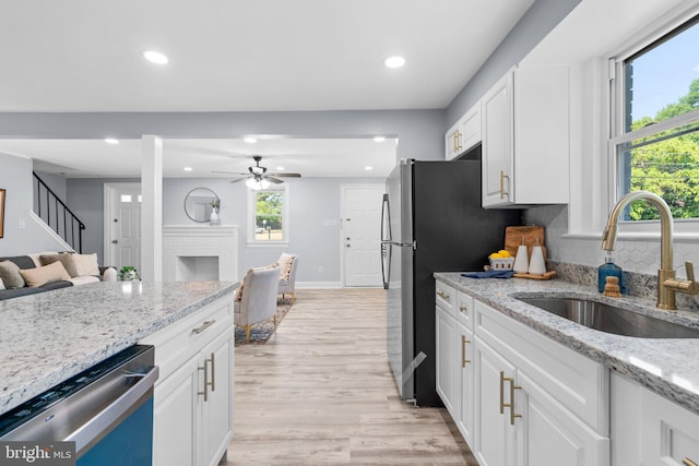 kitchen featuring light stone countertops, white cabinets, stainless steel appliances, sink, and light hardwood / wood-style flooring