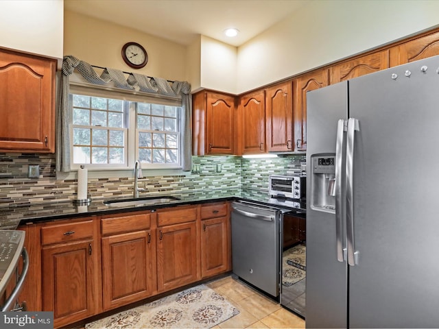 kitchen with light tile patterned floors, stainless steel appliances, decorative backsplash, dark stone countertops, and sink