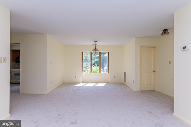 empty room featuring light colored carpet and an inviting chandelier