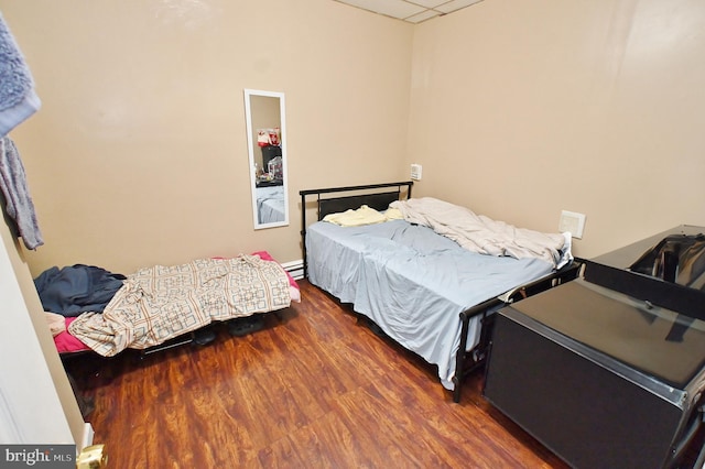 bedroom featuring a drop ceiling, a baseboard radiator, and dark hardwood / wood-style floors