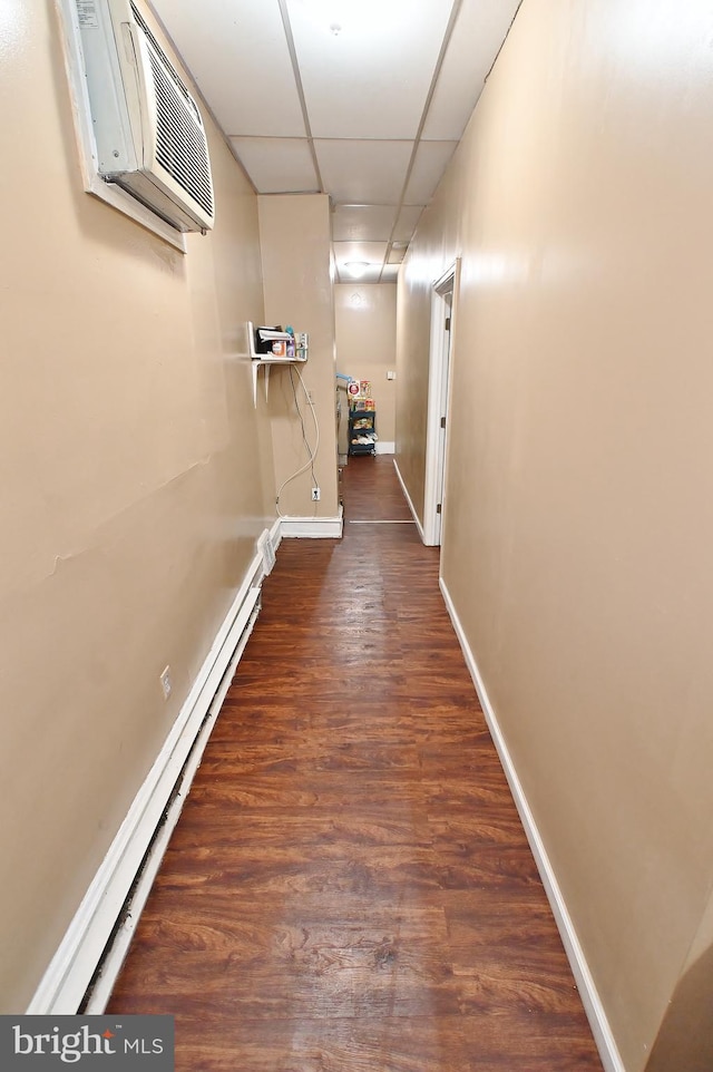 hall with an AC wall unit, dark hardwood / wood-style flooring, a drop ceiling, and baseboard heating