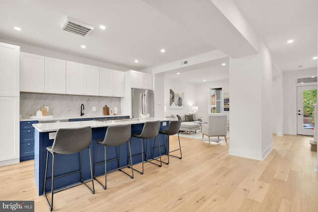 kitchen with white cabinetry, a large island, stainless steel fridge, a breakfast bar area, and decorative backsplash