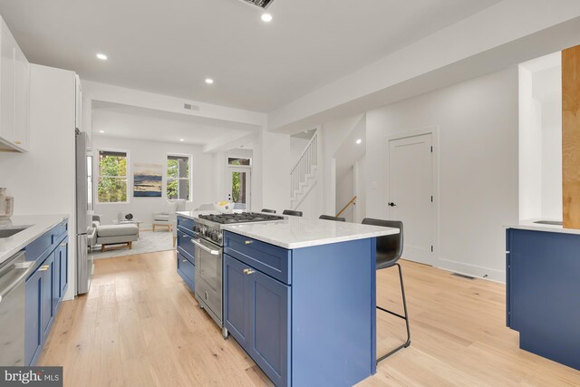 kitchen featuring a breakfast bar, blue cabinets, light hardwood / wood-style flooring, appliances with stainless steel finishes, and white cabinetry