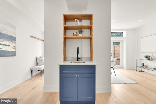 bar with blue cabinetry, sink, and light hardwood / wood-style flooring