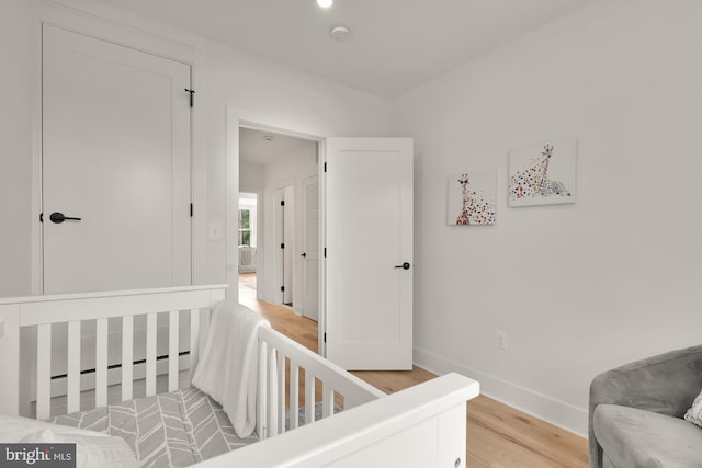 bedroom with wood-type flooring, a baseboard radiator, and a nursery area