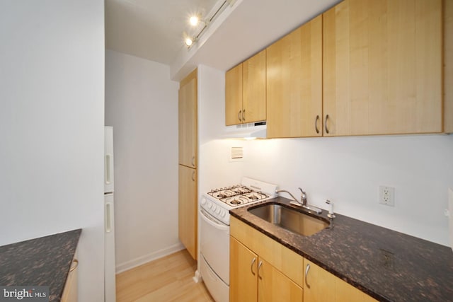 kitchen featuring dark stone countertops, sink, white range, and light brown cabinets