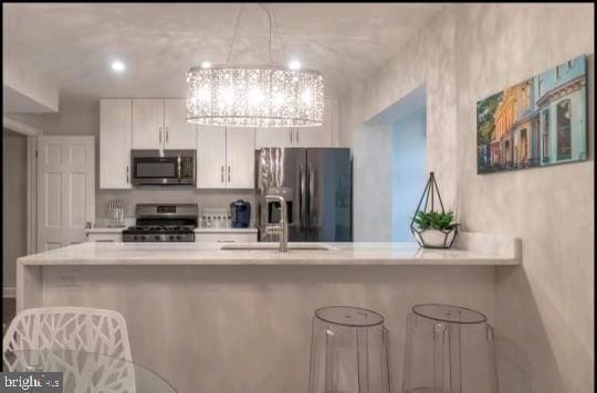 kitchen with sink, appliances with stainless steel finishes, white cabinetry, kitchen peninsula, and a chandelier