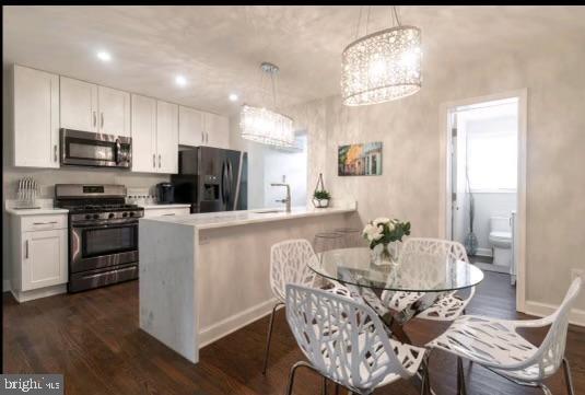 kitchen featuring kitchen peninsula, decorative light fixtures, stainless steel appliances, and white cabinetry