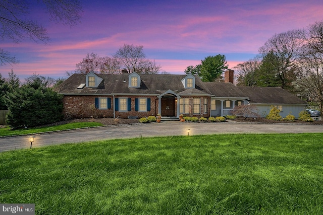 cape cod home featuring a lawn