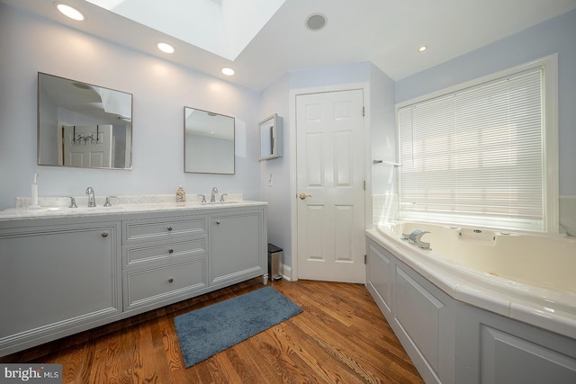 bathroom with a skylight, a bathtub, vanity, and wood-type flooring