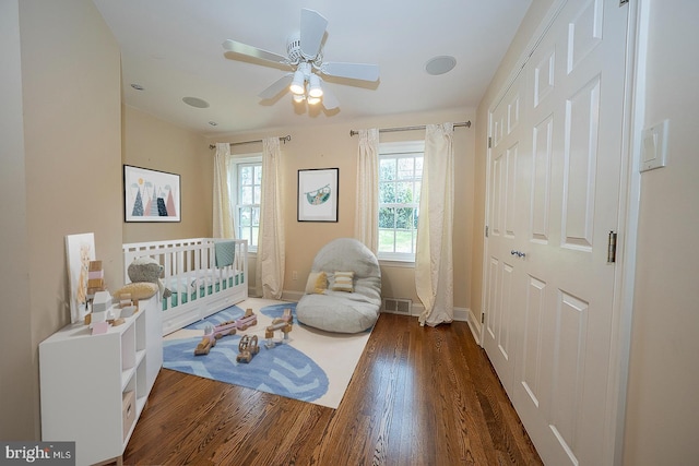 bedroom featuring multiple windows, ceiling fan, a nursery area, and dark wood-type flooring